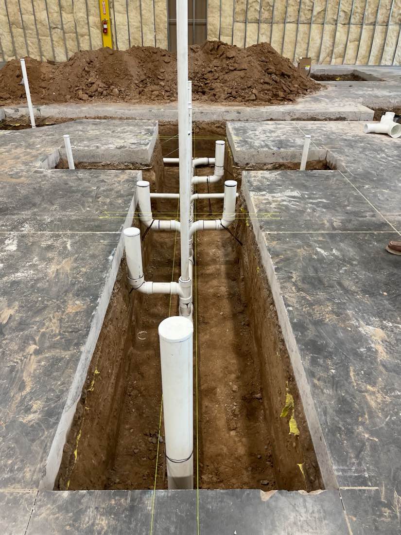 Under-slab rough-in trench with a sleeved vertical riser through a concrete deck.