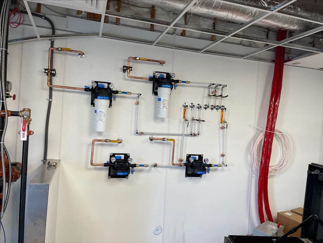 Commercial water filtration and backflow assembly built in copper on a white wall.
